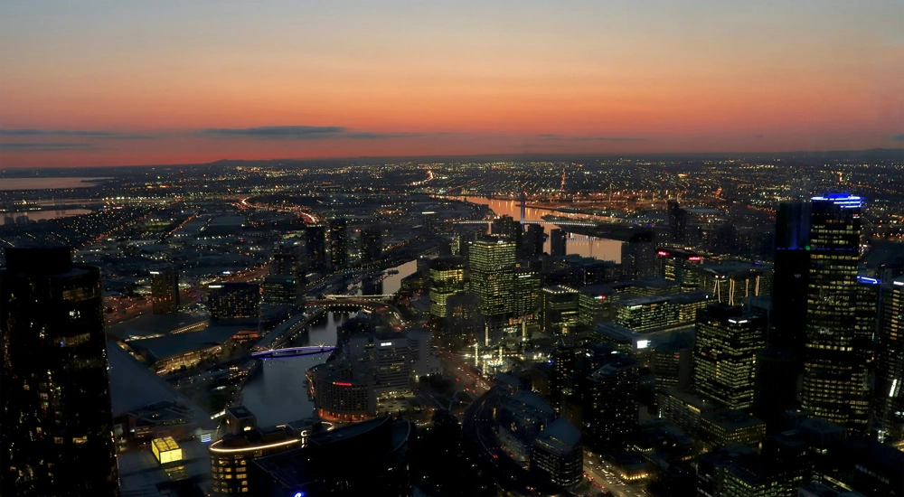 A breathtaking aerial view of Sydney's skyline at sunset, showcasing towering skyscrapers, a glowing sky, and serene waters in the distance