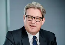 Murray Rowden, Global Head of Infrastructure, standing outside in front of an outdoor urban setting, featuring modern architectural elements with clean lines. There are hints of greenery, suggesting some trees or plants.