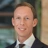Portrait of Dennis de Wolf, Director, Real Estate, outside in front of a blurred brown background featuring a building and mix of natural and urban elements.