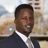 Portrait of Henry Wambaa, Project Manager, outside in front of a blurred brown background featuring a building and mix of natural and urban elements.