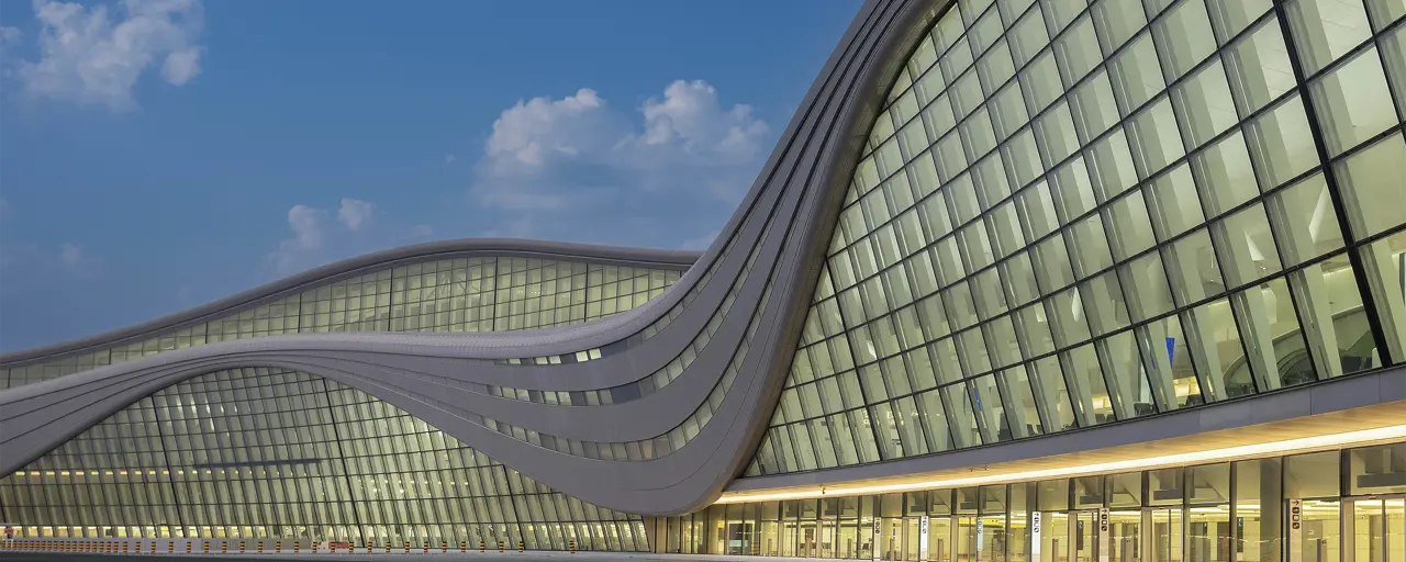 Modern, curved glass building with yellow lights aglow inside 