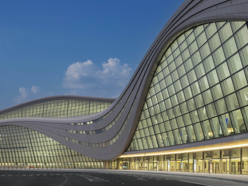 Modern, curved glass building with yellow lights aglow inside
