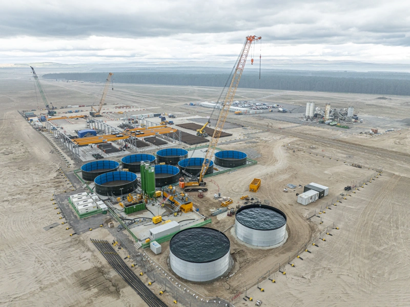 Aerial view of port buildings and storage facilities under construction in the foreground, looking out towards the sea in the distance