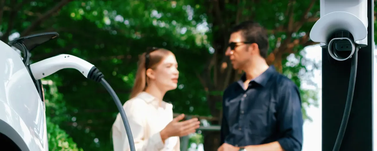 Man and woman standing and talking whilst charging white electric cars