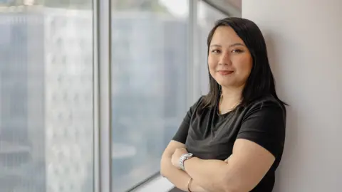 Portrait of Siti Norman, Director, Digital, Singapore, standing against white background and window.