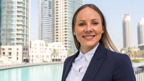 Portrait of Kaarin Kalavus, Director, Abu Dhabi, outside in front of water stream and tall city buildings
