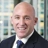 Portrait of Simon Kearney, Director - Real estate, with city landscape featuring building with lots of windows in the background.