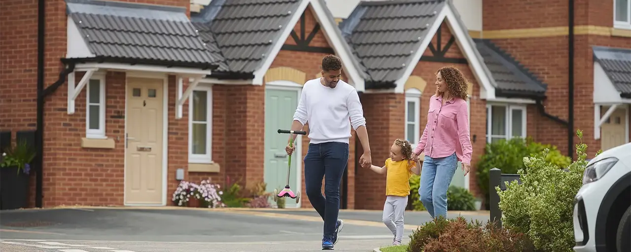 Two adults holding the hand of a child in yellow top outside of housing estate 