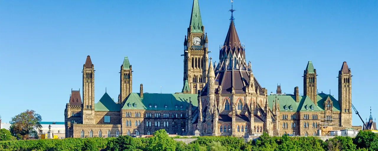 Parliament building in Ottawa, Canada with clock tower flying Canadian flag against a blue sky