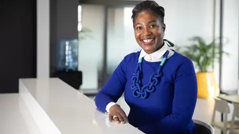 Portrait of Hazel Kannemeyer, Associate Director, Project Management, South Africa, sitting in office space in blue sweater.