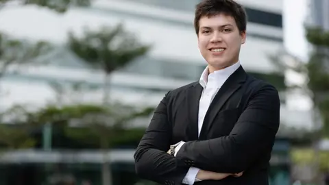 Vincent Tameeris, Assistant Consultant, Singapore, standing outside an office with his arms folded, smiling