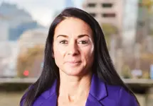 Portrait of Faye Banks, Director, Transmission and Distribution, UK, standing outside featuring an urban cityscape with tall buildings and a mix of architectural styles. The scene includes some trees with autumn foliage, adding a touch of color. 