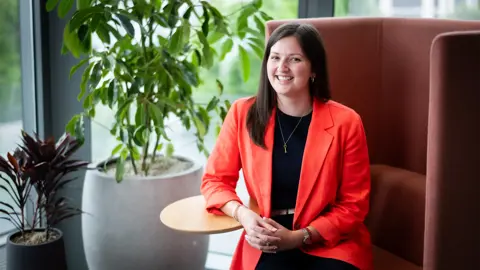 Portrait of Halle Stewart, Associate Director, Asia Regional Sector Lead, Singapore, sitting in office space next to a plant.