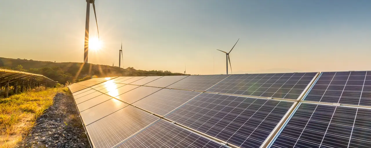 View across a field of solar panels in the foreground with wind turbines in the background