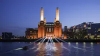 A striking image of London's iconic Battersea Power Station against a blue night sky. The industrial columns are lit up and light also shines on the water in front. To the right of the building are a block of modern, glass fronted flats. 