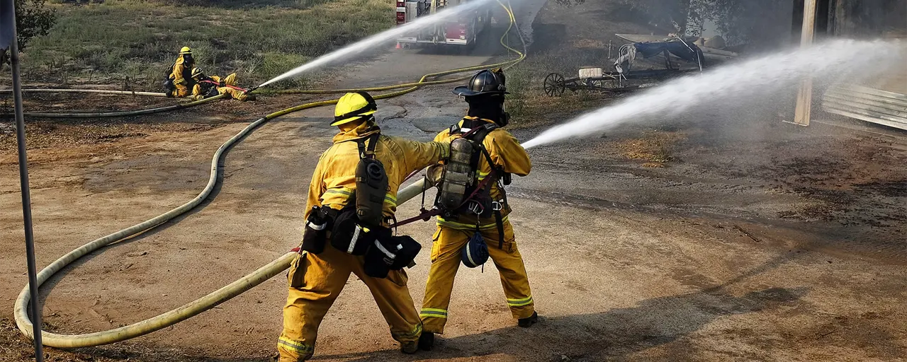 Fire fighters in yellow suits using a water hose