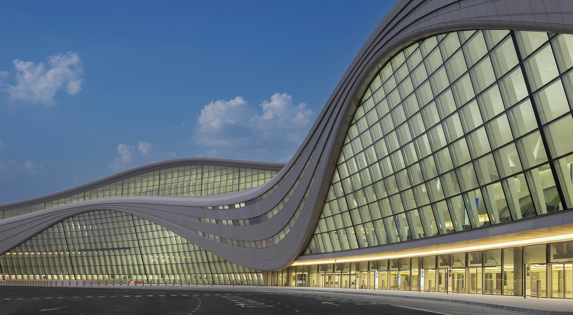 Curved glass airport terminal building with yellow lights lit up inside