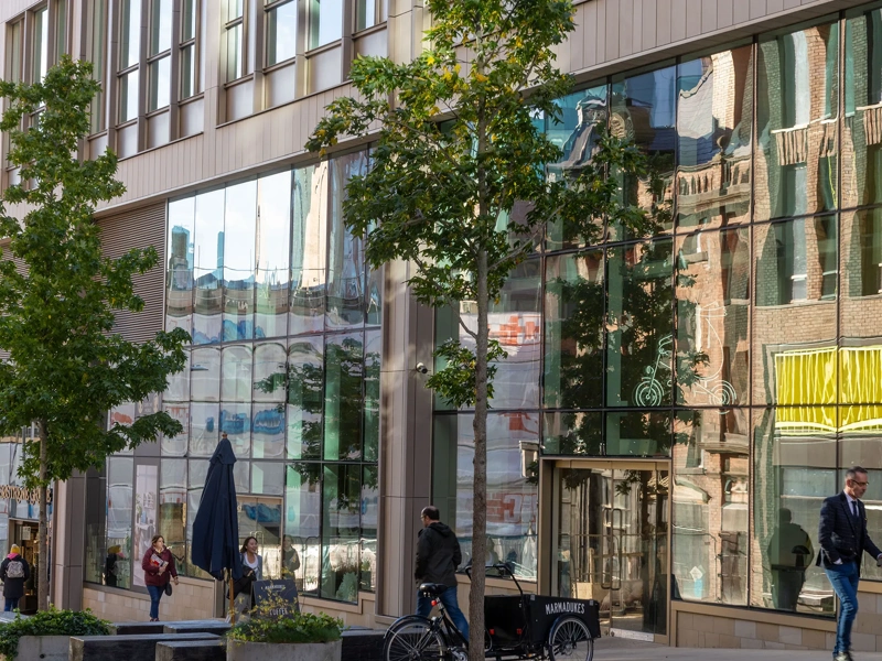 Image of glass window building with trees in front of it and people walking by