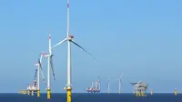 Big white wind turbines in sea water against blue sky.