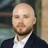 Portrait of Kevin Higgins, Lead Cost Manager, outside in front of a blurred brown background featuring a building and mix of natural and urban elements.