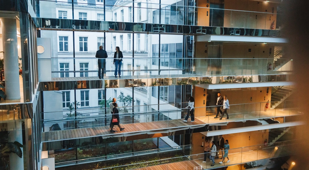 Open multi-storey office atrium with glass walkways and people walking between floors.