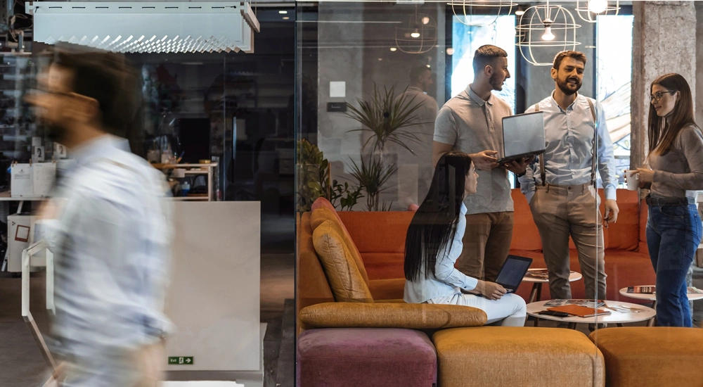 Colleagues standing around in a colourful based office, engaged in a conversation.