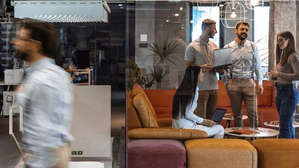 Colleagues standing around in a colourful based office, engaged in a conversation.