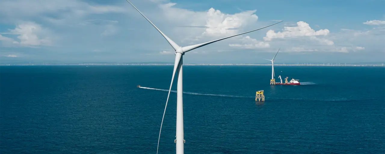 Daytime aerial view of an offshore wind turbine in the foreground with further turbines in the distance