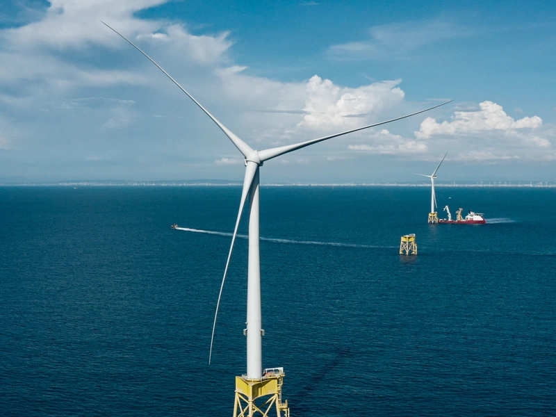 Daytime aerial view of an offshore wind turbine in the foreground with further turbines in the distance