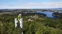 Mobile 5G installation, with man in hi vis on top of 5G tower, surrounded by trees