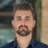 Portrait of Jay Figg, Senior Project Manager, Infrastructure, outside in front of a blurred brown background featuring a building and mix of natural and urban elements.