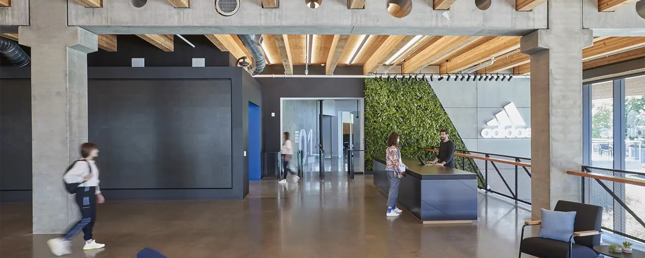 Modern Adidas offices with wooden interior and two people walking while a woman talks to a man at a reception desk