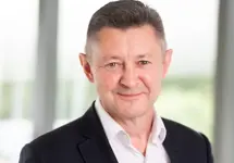 Portrait of Ed Robinson, Global Defence Lead, Standing in a glass office.