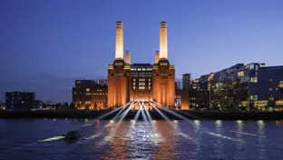 Battersea Power Station lit up at night, view from the Thames with buildings in the background