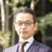 Portrait of Yoshihiro Kumano, Senior Project Manager, standing outside in front of tree branches in navy suit.