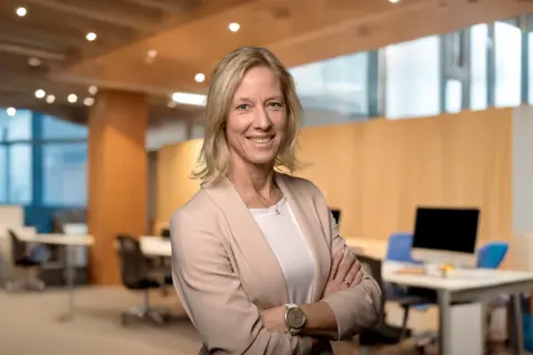 Portrait of Bettina Würfel, Managing Director, standing in an office with warm wooden backdrop and windows