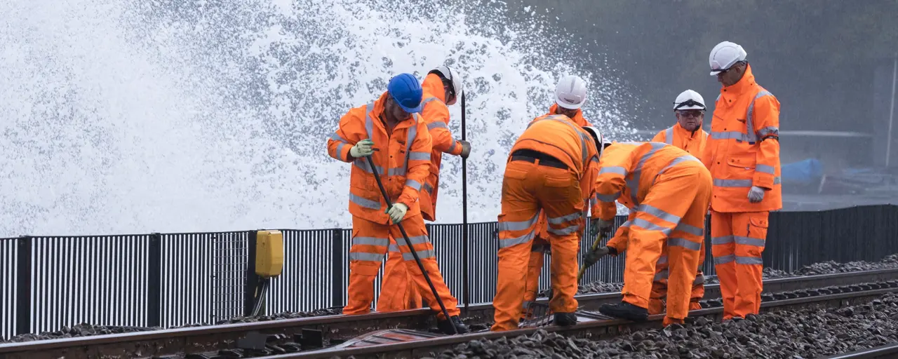 Workers wearing orange high vis working on a train track with water splashing