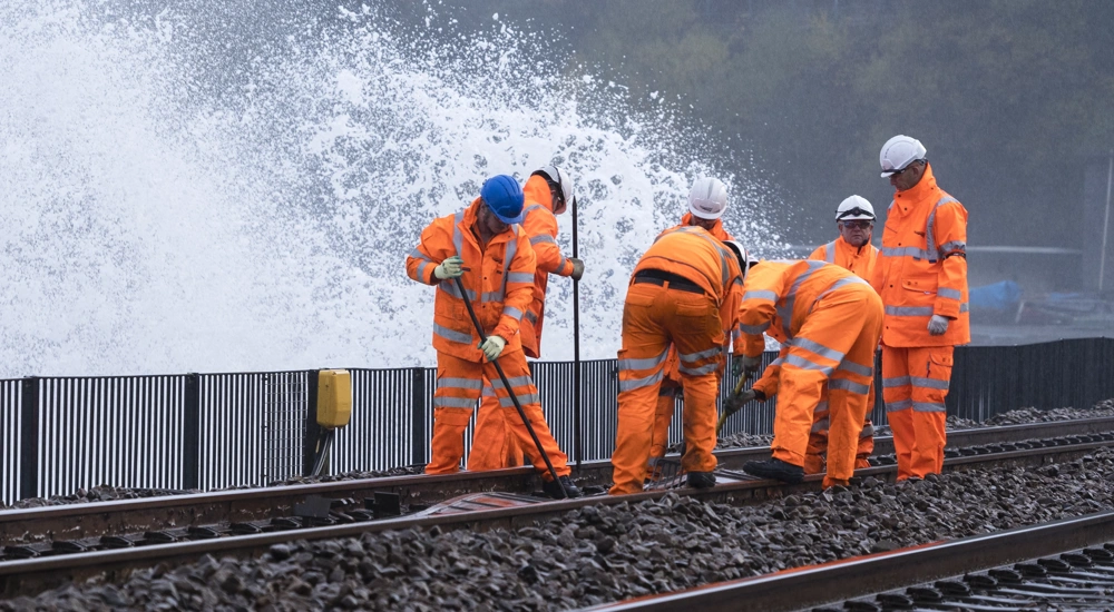 Workers wearing orange high vis working on a train track with water splashing